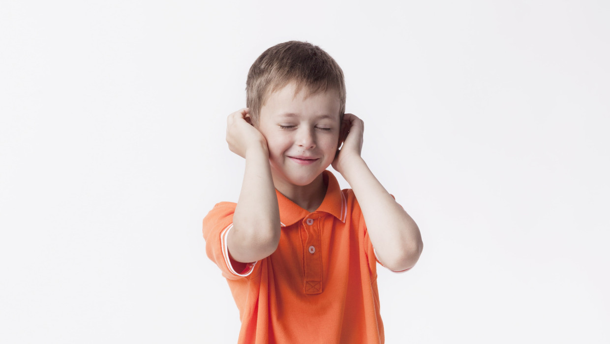 Niño con los ojos cerrados tapándose los oídos